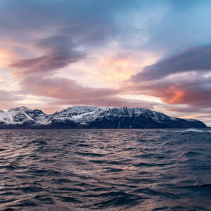 Small boat crossing the fjord below snowy mountains at dusk, Kvænangen, Troms, Norway