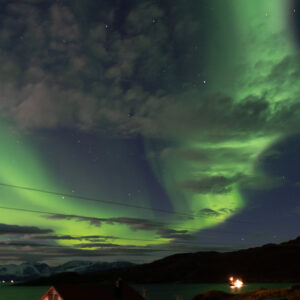 Aurore boréale verte et étoiles au-dessus d’une maison éclairée, cadrage vertical, Seglvik, Troms, Norvège