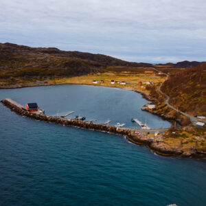 Aerial view of a curved harbour pier and coastal hamlet in autumn colours, Seglvik, Troms, Norway