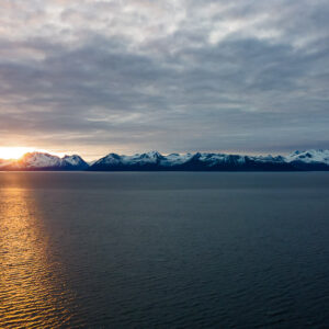 Aerial view of sunset reflecting on the fjord below snowy mountains, Seglvik, Troms, Norway