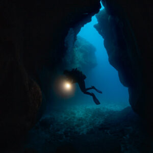 Plongeuse avec phare en silhouette à l’entrée d’une grotte, cadrage vertical, Flic-en-Flac, île Maurice