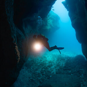 Plongeuse avec phare éclatant dans l’entrée d’une grotte, cadrage vertical serré, Flic-en-Flac, île Maurice