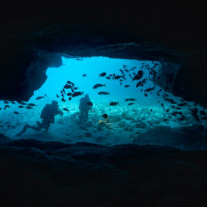 Deux plongeurs dans une large ouverture de grotte avec des silhouettes de poissons, Flic-en-Flac, île Maurice