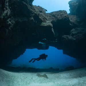 Diver framed under a wide rock arch on sandy floor, wider view, Flic-en-Flac, Mauritius