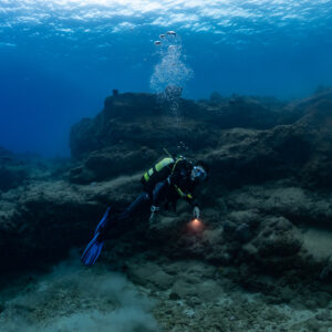 Plongeuse avec phare au pied d’une formation rocheuse, bulles montantes, Flic-en-Flac, île Maurice
