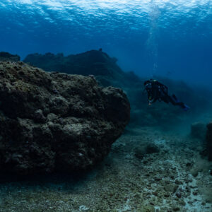 Diver swimming between large rock formations in blue water, Flic-en-Flac, Mauritius