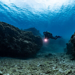 Diver with red torch in a channel between rocks under the surface, Flic-en-Flac, Mauritius