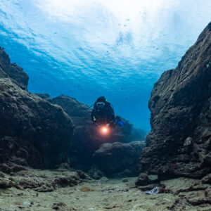 Diver with torch facing the camera in a narrow channel between rocks, Flic-en-Flac, Mauritius