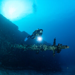 Diver with a torch beside a wreck mast lying horizontally, Maldives