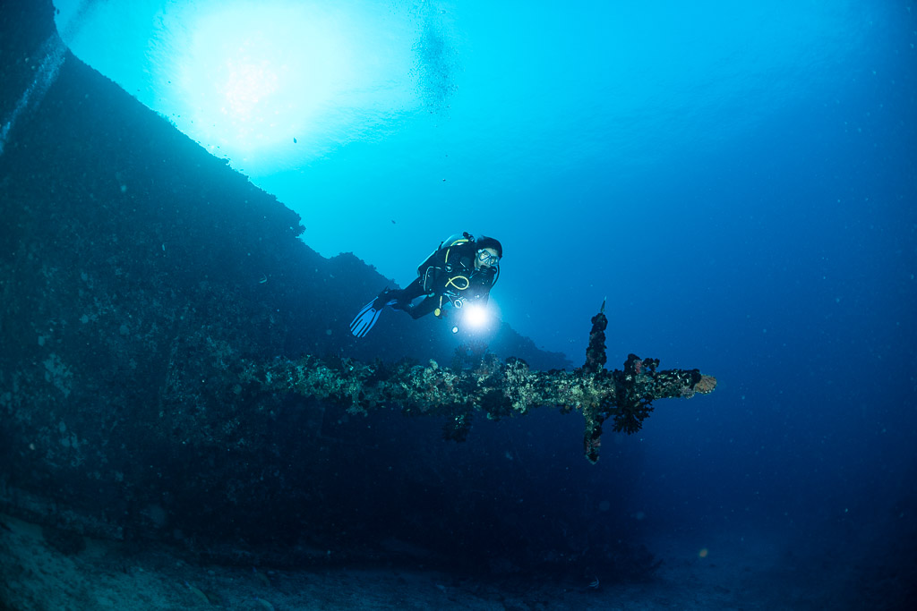 Diver with a torch beside a wreck mast lying horizontally, Maldives