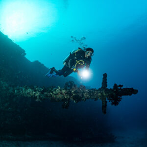 Diver lighting a coral-encrusted mast on the wreck, closer view, Maldives