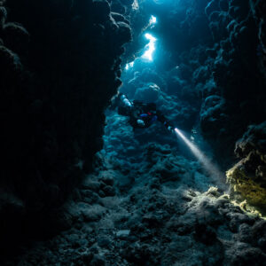 Rebreather diver deep in a cave fissure, light pouring through, Zabargad, Red Sea, Egypt