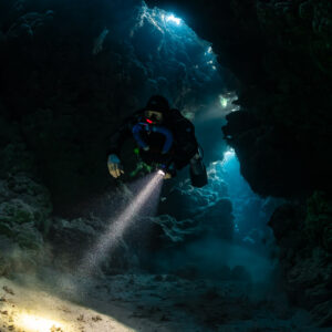 Rebreather diver emerging from the cave darkness with torch, Zabargad, Red Sea, Egypt