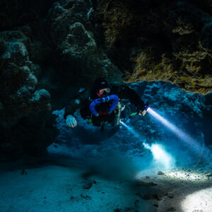 Rebreather diver with two torches beams in the cave, Zabargad, Red Sea, Egypt