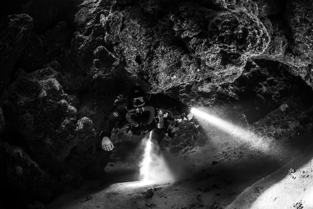 Rebreather diver with torches in the cave, black and white, Zabargad, Red Sea, Egypt
