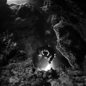 Rebreather diver framed by a cave opening, black and white, Zabargad, Red Sea, Egypt