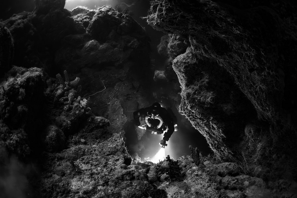 Rebreather diver framed by a cave opening, black and white, Zabargad, Red Sea, Egypt
