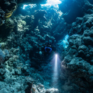 Rebreather diver in a cave gully with a torch beam, Zabargad, Red Sea, Egypt