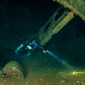 Rebreather diver with torch inside the Levanzo wreck among barrels, Red Sea, Egypt