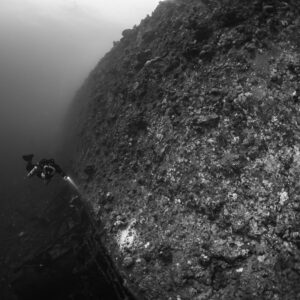 Rebreather diver dwarfed by the hull of the Levanzo wreck, black and white, Red Sea, Egypt