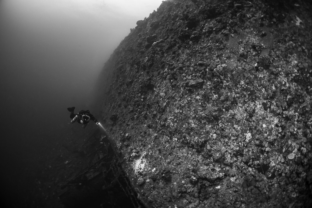 Rebreather diver dwarfed by the hull of the Levanzo wreck, black and white, Red Sea, Egypt