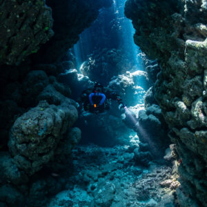 Rebreather diver deep inside a narrow cave fissure lit by sunlight, Gota Jeny, Red Sea, Egypt