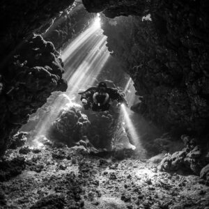 Rebreather diver under sunbeams in a cave, black and white, Gota Jeny, Red Sea, Egypt