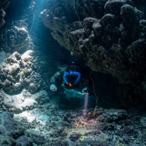 Rebreather diver lighting the cave floor beneath a rocky overhang, Gota Jeny, Red Sea, Egypt