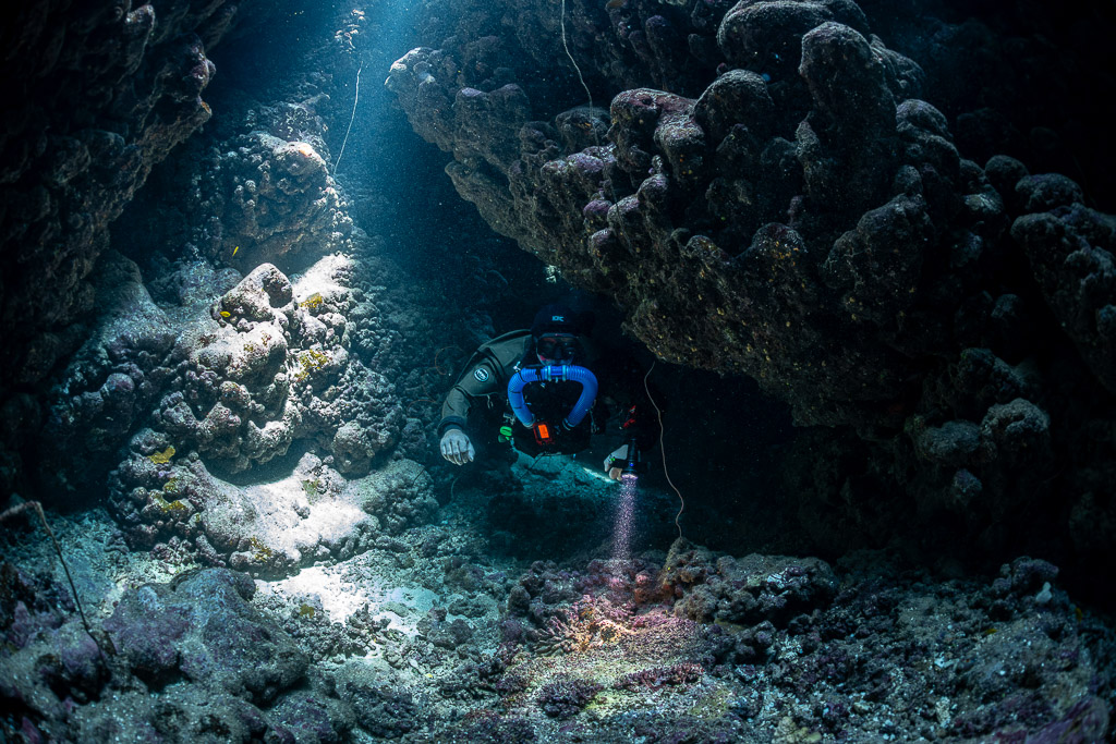 Rebreather diver lighting the cave floor beneath a rocky overhang, Gota Jeny, Red Sea, Egypt