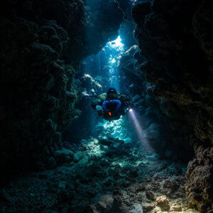 Rebreather diver in the heart of a dark cave, distant light shafts, Gota Jeny, Red Sea, Egypt