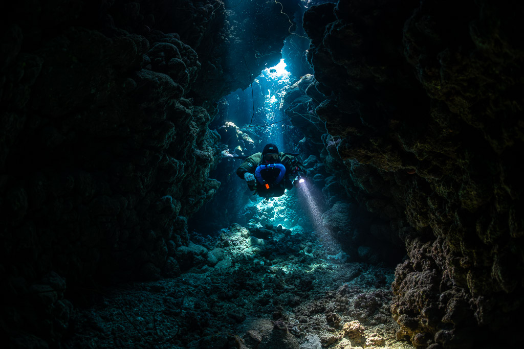 Rebreather diver in the heart of a dark cave, distant light shafts, Gota Jeny, Red Sea, Egypt