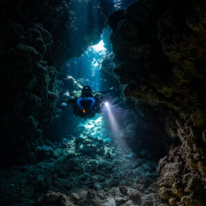 Rebreather diver below a cave chimney lit from the surface, Gota Jeny, Red Sea, Egypt