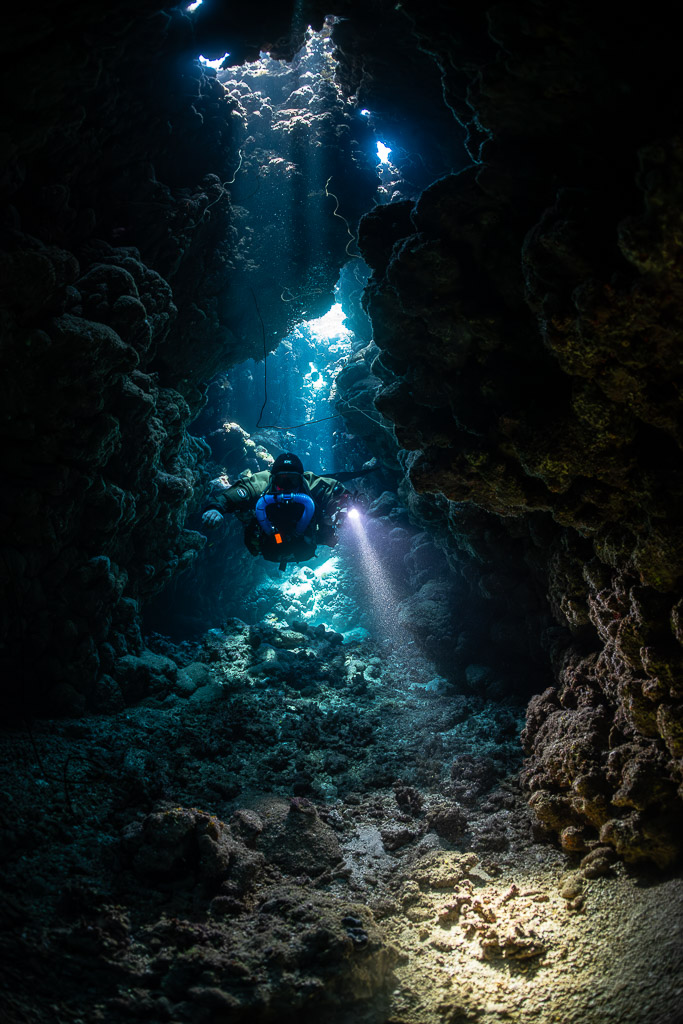 Rebreather diver below a cave chimney lit from the surface, Gota Jeny, Red Sea, Egypt