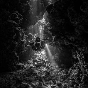 Rebreather diver below a cave chimney, black and white, Gota Jeny, Red Sea, Egypt