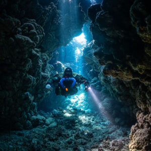 Rebreather diver rising through a light-filled cave chimney, Gota Jeny, Red Sea, Egypt