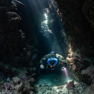 Rebreather diver in a narrow cave corridor with light from above, Gota Jeny, Red Sea, Egypt