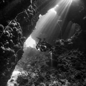 Rebreather diver under a burst of sunbeams in a cave, black and white, Gota Jeny, Red Sea, Egypt