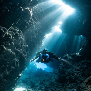 Rebreather diver beneath a jagged cave opening flooded with light, Gota Jeny, Red Sea, Egypt