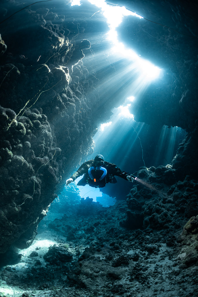 Rebreather diver beneath a jagged cave opening flooded with light, Gota Jeny, Red Sea, Egypt