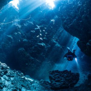 Rebreather diver small in a vast cave hall pierced by sunbeams, Gota Jeny, Red Sea, Egypt
