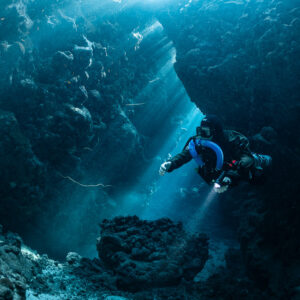 Rebreather diver gliding through sunbeams in a cave hall, Gota Jeny, Red Sea, Egypt