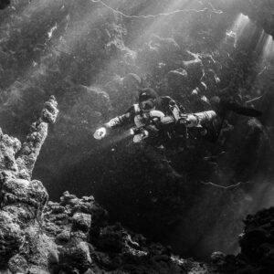 Rebreather diver crossing sunbeams in a cave hall, black and white, Gota Jeny, Red Sea, Egypt