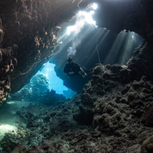 Diver at a cave exit opening onto the blue reef, Gota Jeny, Red Sea, Egypt