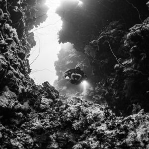 Rebreather diver at a cave mouth in the reef, black and white, Abu Kebrita, Red Sea, Egypt