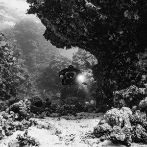 Rebreather diver beneath a coral overhang, black and white, Habili Gafar and Umm Aruk, Red Sea, Egypt