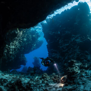 Rebreather diver entering Saint John's Cave beneath a rock arch, Saint John's Cave, Red Sea, Egypt