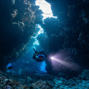Rebreather diver with a bright torch in the main cave passage, Saint John's Cave, Red Sea, Egypt
