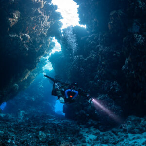 Rebreather diver with torch in a cave passage, Saint John's Cave, Red Sea, Egypt