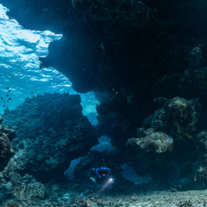 Rebreather diver small at the far end of the cave entrance, Saint John's Cave, Red Sea, Egypt