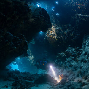 Rebreather diver in a cave passage with light holes in the ceiling, Saint John's Cave, Red Sea, Egypt
